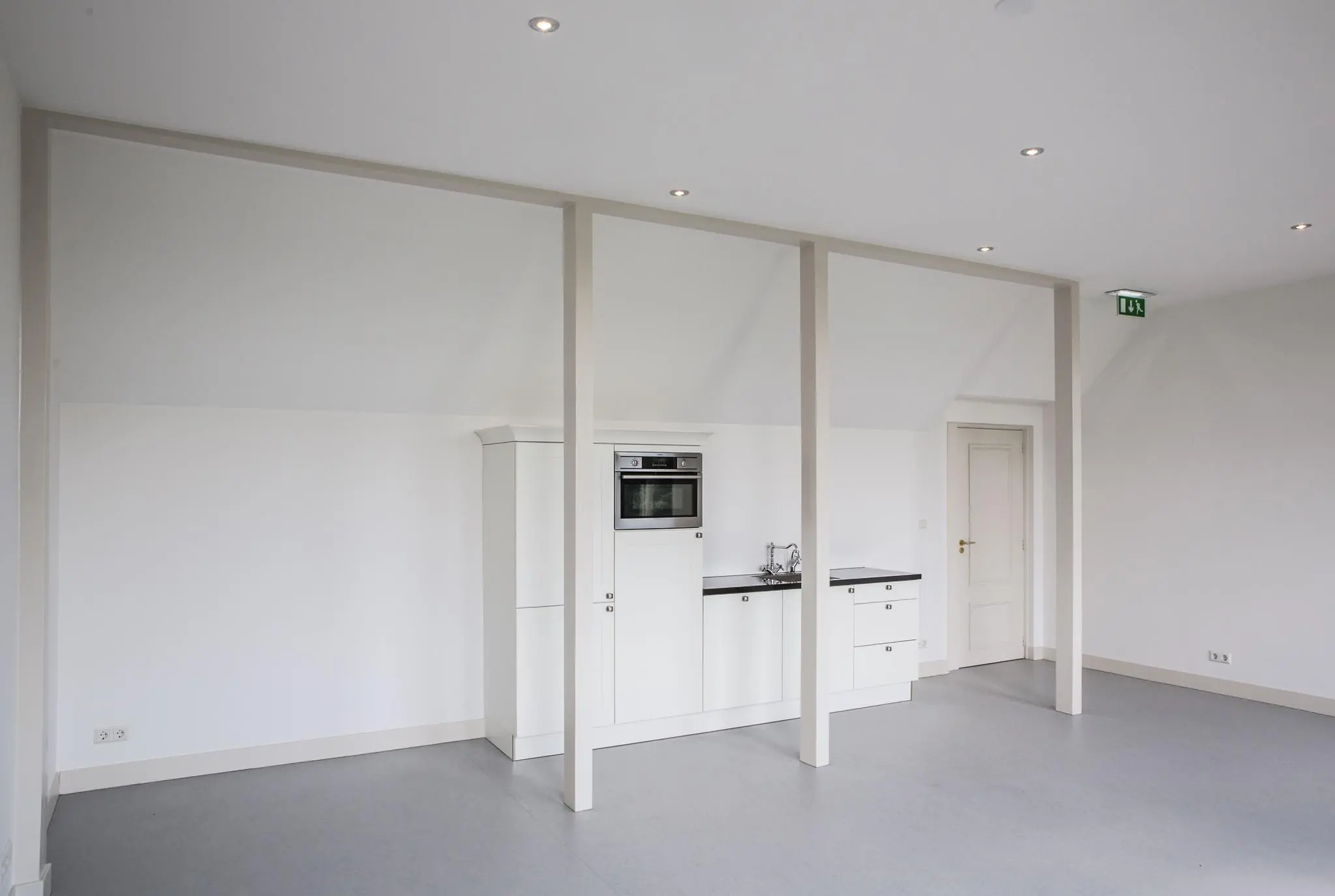 Moderne, witte kitchenette met inbouwapparatuur in een minimalistische ruimte aan de Naarderstraat.