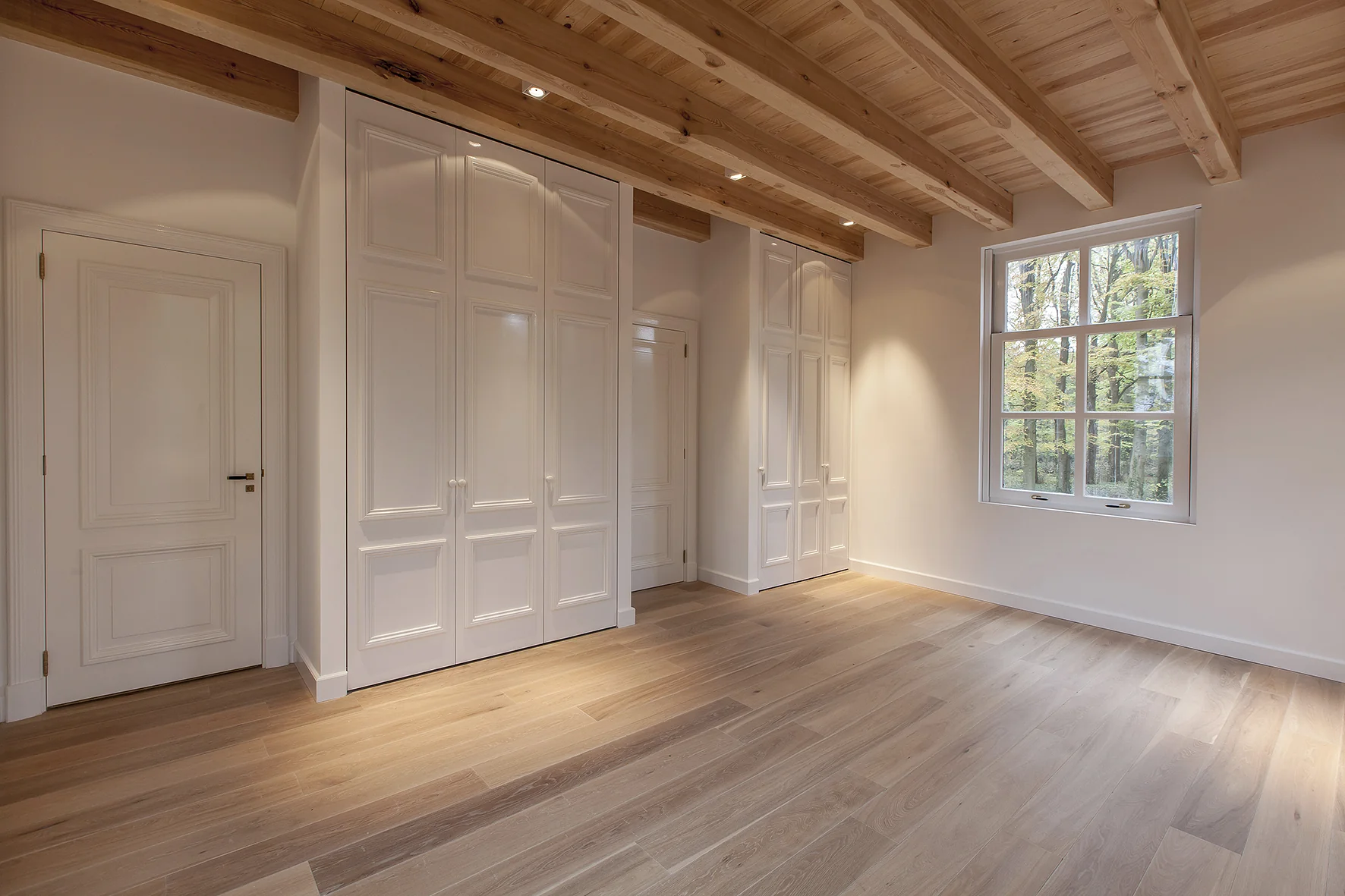 Lichte, lege kamer aan de Naarderstraat met houten vloer, ingebouwde kasten, houten balkenplafond en een raam met uitzicht op bomen.
