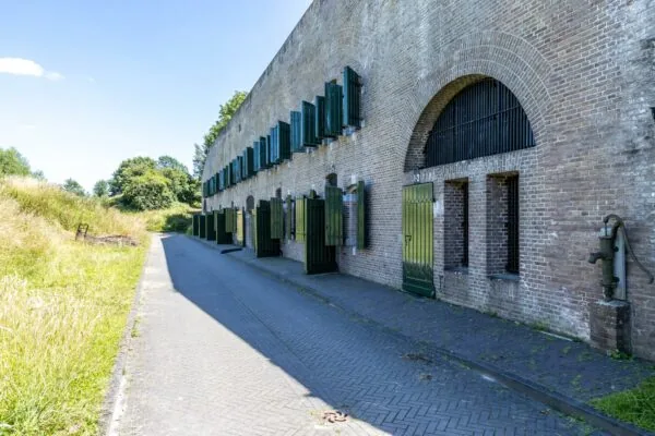 Bakstenen fortgebouw aan de Fortweg met groene deuren en luiken langs een smal geplaveid pad.