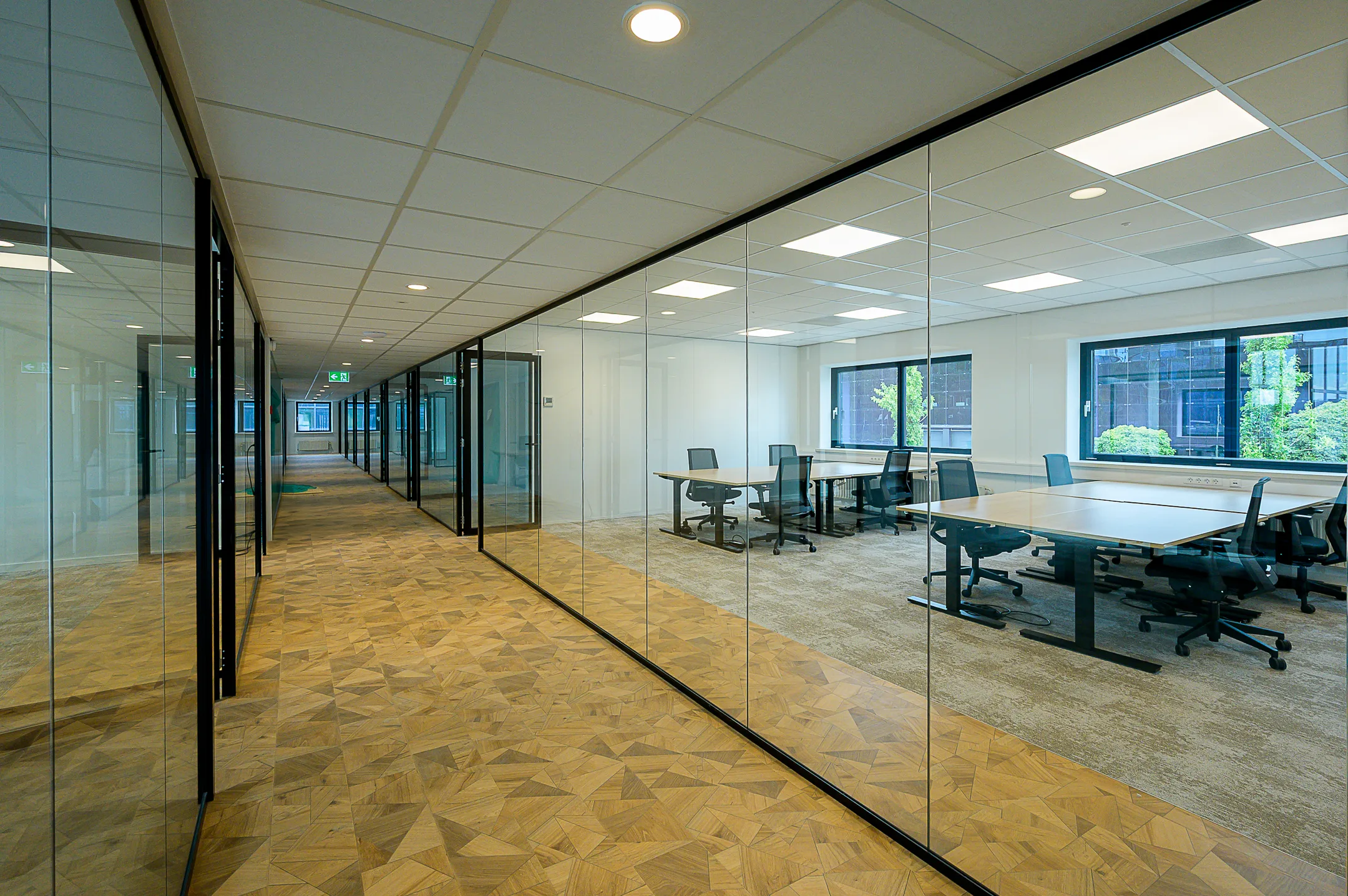Een moderne kantoorruimte met glazen wanden en bureaus met bureaustoelen.