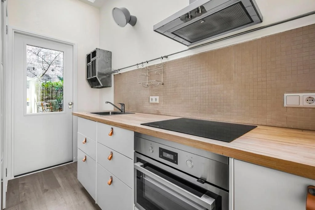 Moderne, smalle keuken aan de Westerstraat met houten aanrechtblad, inductiekookplaat en strakke afwerking.
