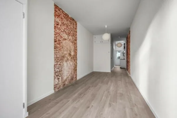 Langwerpige gang met houten vloer, witte muren en decoratieve bakstenen accenten in een woning aan de Westerstraat.