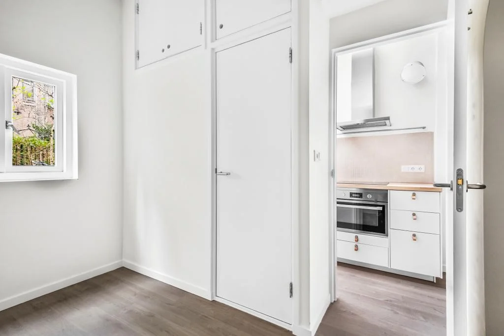 Licht interieur met witte kasten en een doorkijk naar een moderne keuken in een woning aan de Westerstraat.