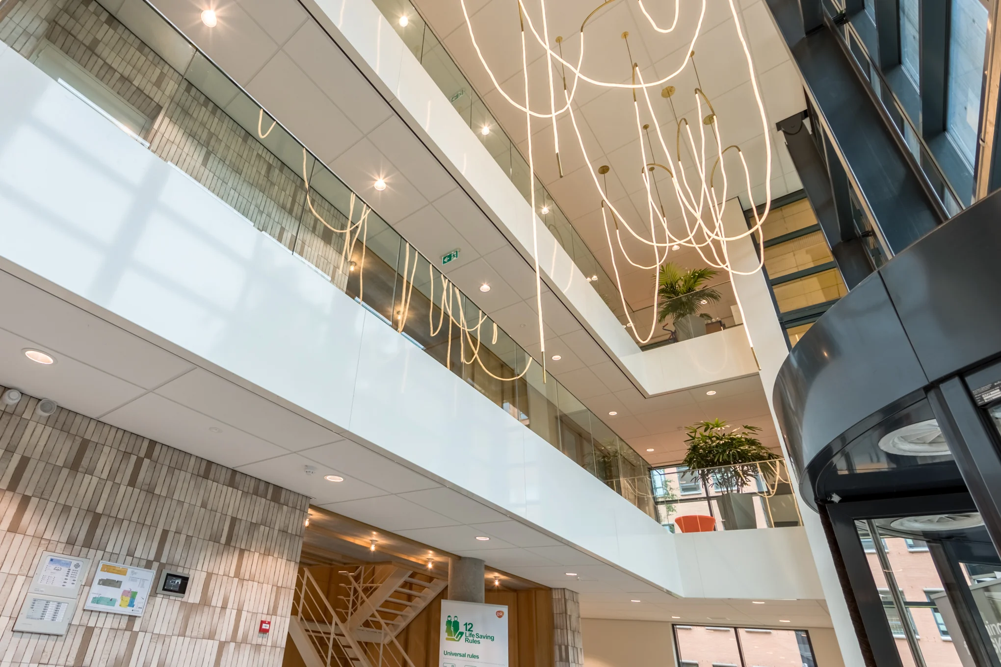 Modern atrium van een kantoorgebouw aan de Hullenbergweg met glazen balustrades, hangende designverlichting en grote raampartijen.
