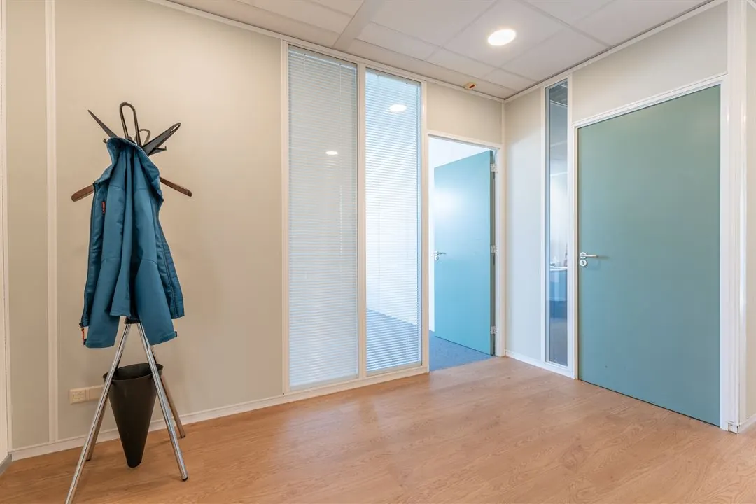 Een moderne hal met houten vloer, blauwe deuren en een kapstok met een blauwe jas.