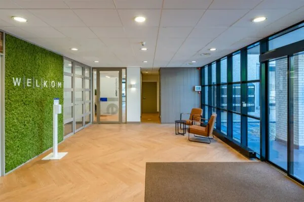 Ingang van een modern kantoor met een groene moswand en een uitnodigend welkomsbord.