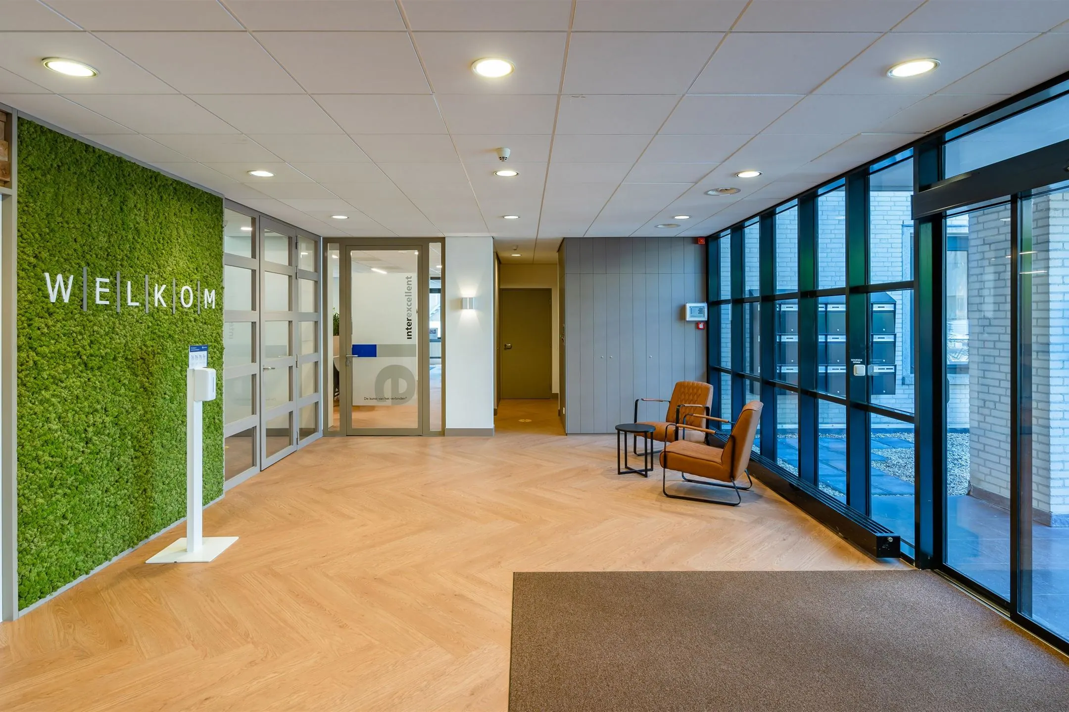 Ingang van een modern kantoor met een groene moswand en een uitnodigend welkomsbord.