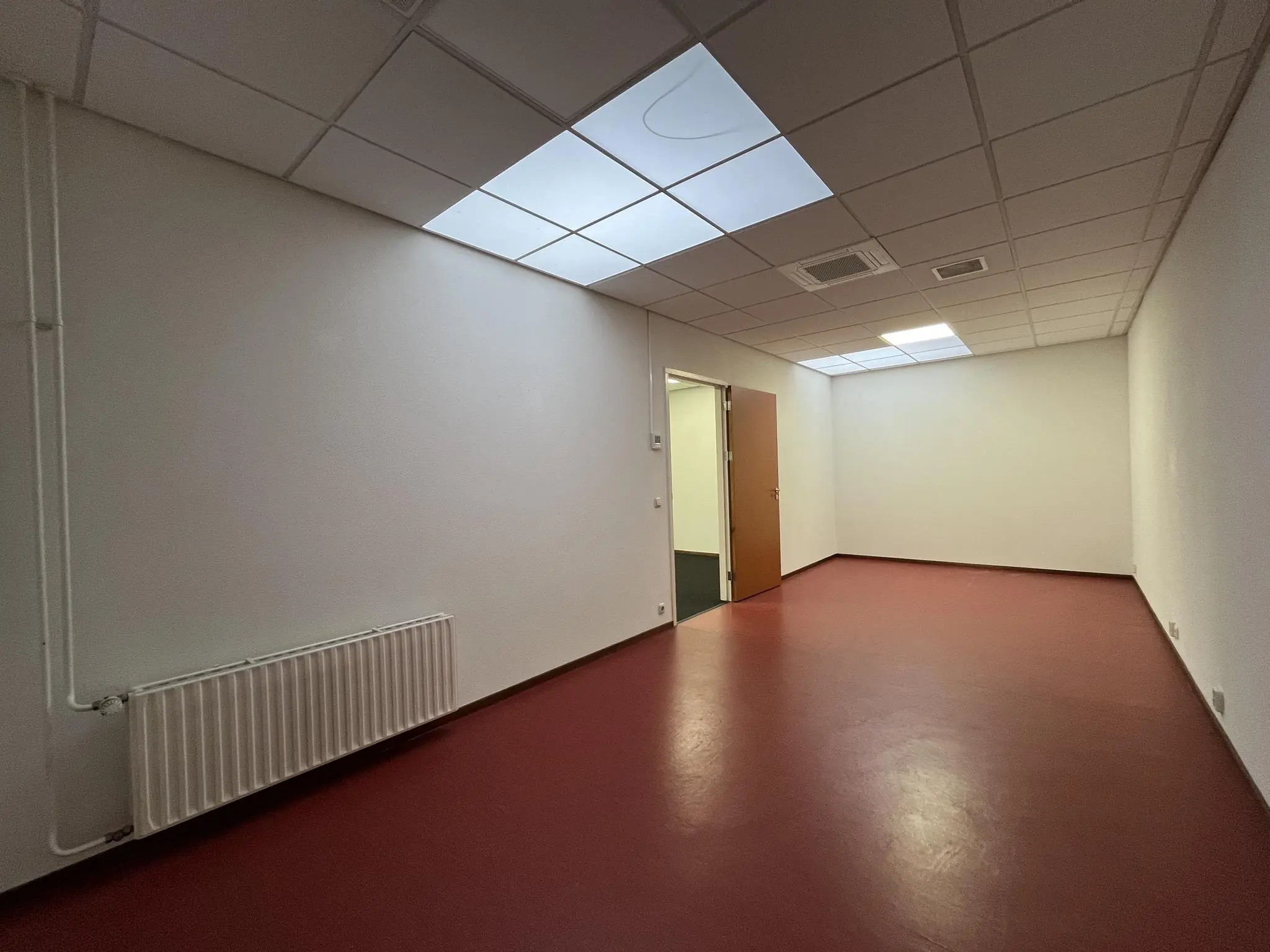 Lege kantoorruimte aan de Kwekerijweg met rode vloer, systeemplafond en openstaande houten deur.