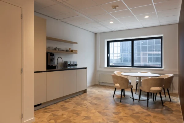 Een moderne kantoorruimte met keukenhoek, ronde tafel en vier stoelen.
