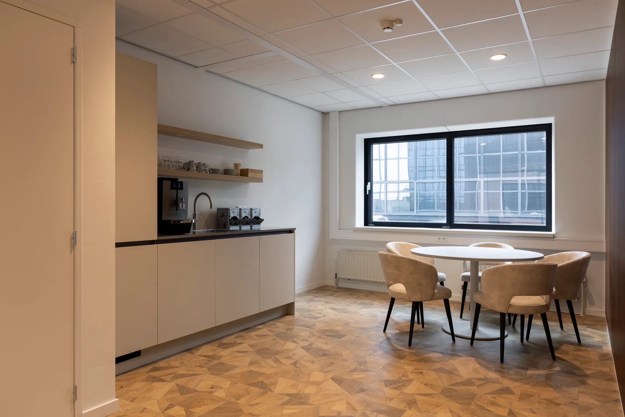 Een moderne kantoorruimte met keukenhoek, ronde tafel en vier stoelen.