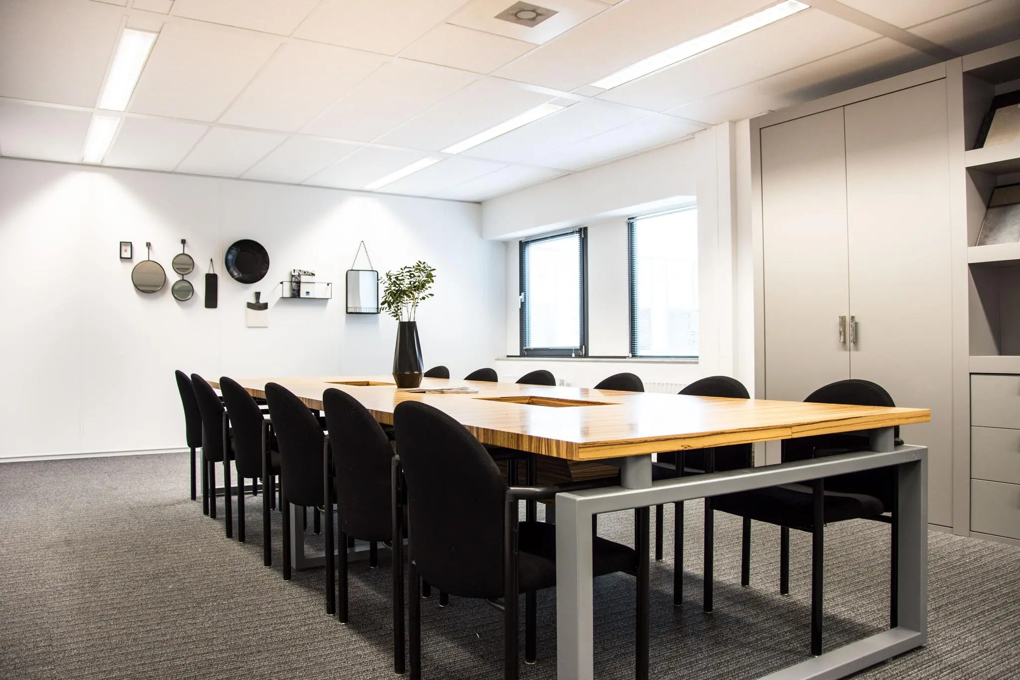 Vergaderruimte met een houten tafel, zwarte stoelen en moderne wanddecoratie aan de Meidoornkade.