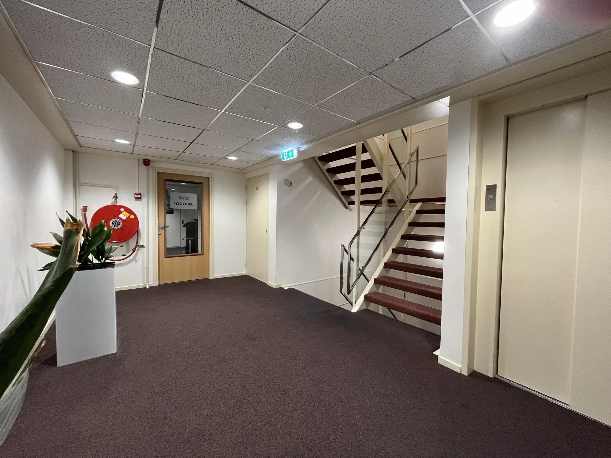 Binnenhal van een kantoorpand aan de Industrieweg met een trap, lift, brandslanghaspel en een deur naar kantoorruimte van Iivis Incase.