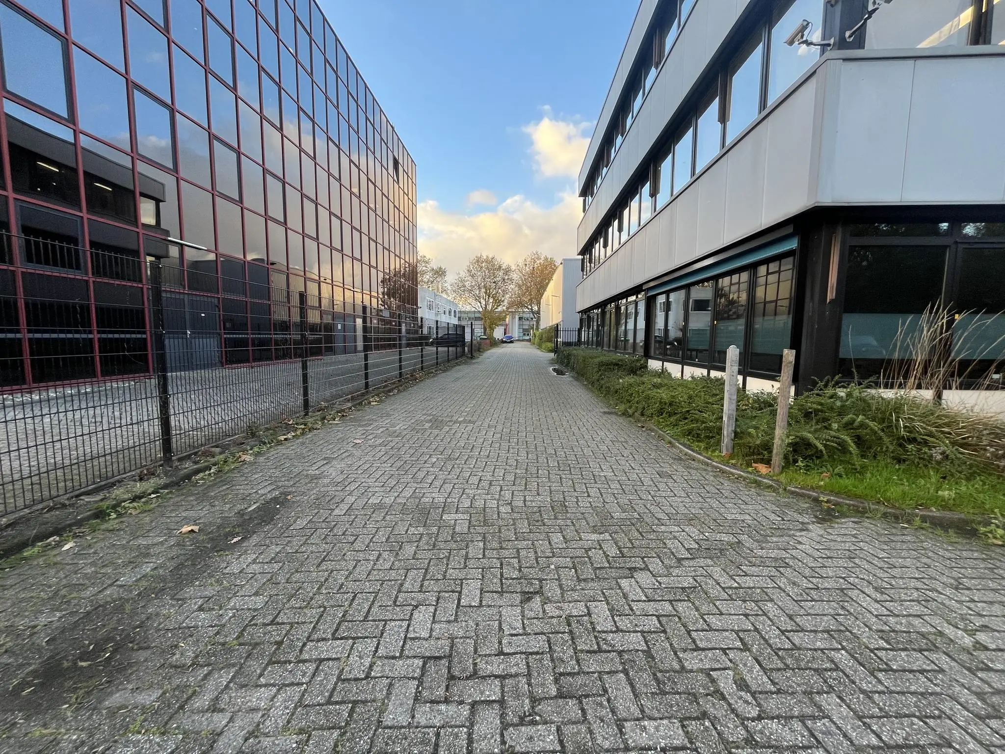 Een smalle, met klinkers bestrate weg tussen twee moderne bedrijfsgebouwen aan de Industrieweg.
