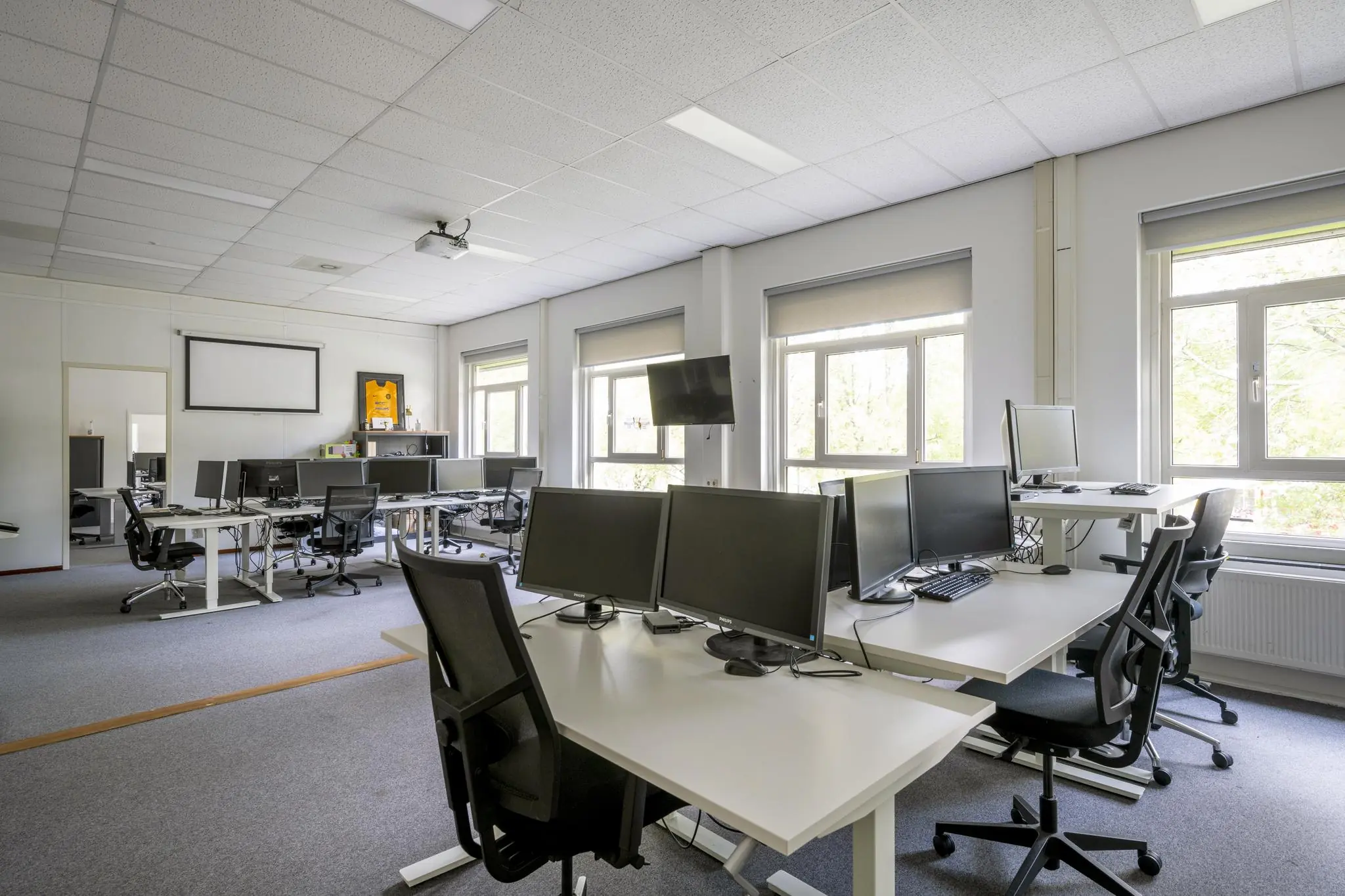 Ruime, moderne kantoortuin aan de Van der Madeweg met meerdere werkplekken, bureaustoelen en computers.