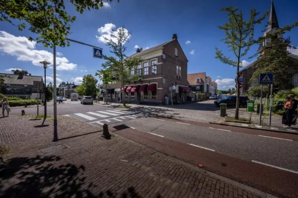 Zonnige straatzicht op de Dorpsstraat met karakteristieke gebouwen, zebrapad en enkele voetgangers.