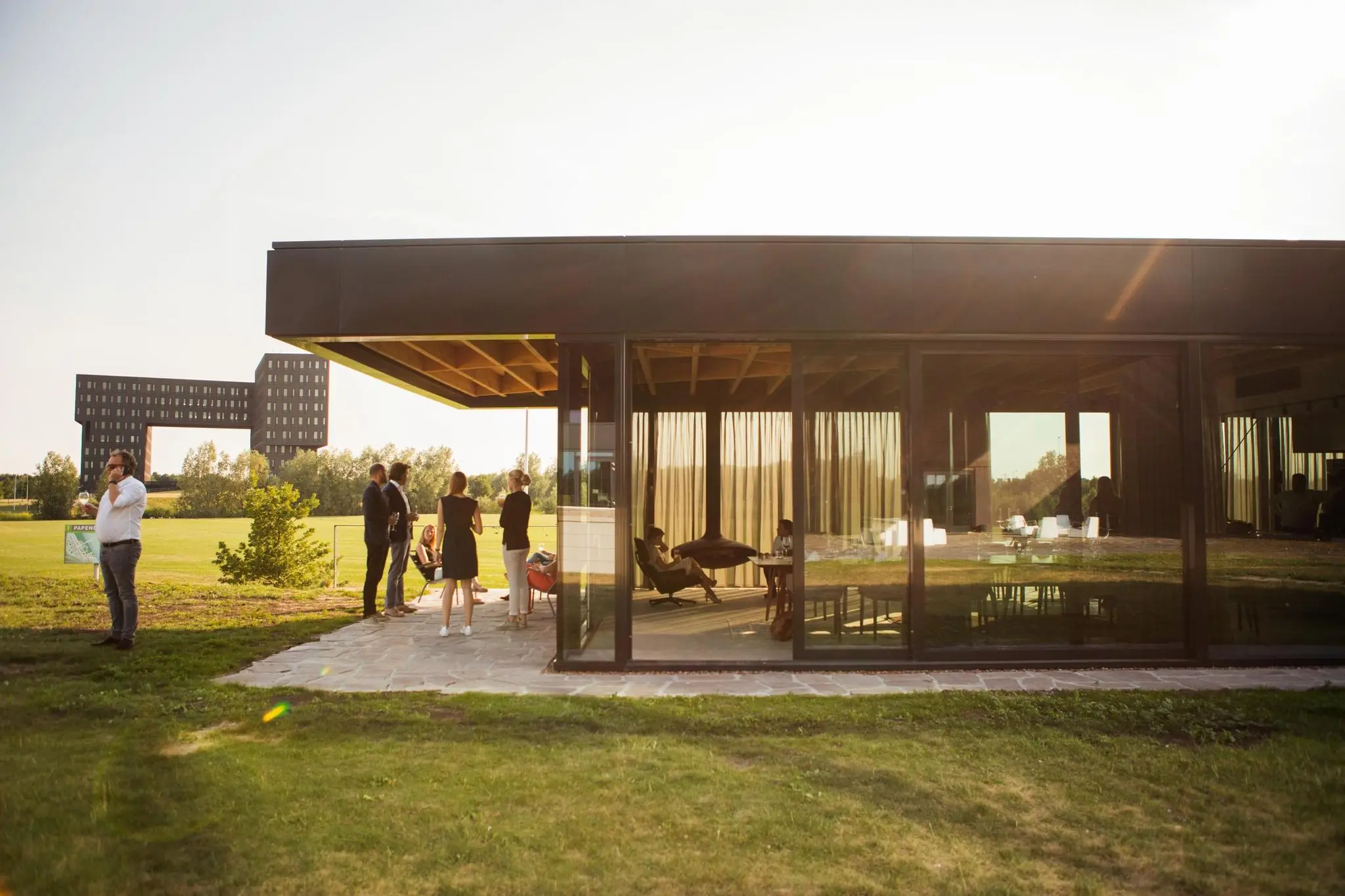 Moderne glazen kantoorpaviljoen aan de Orteliuslaan met groepje mensen buiten op het terras bij zonnig weer.