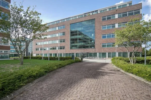 Kantoorgebouw aan de Tupolevlaan met bakstenen gevel, grote glazen entree en omliggende groenvoorziening.