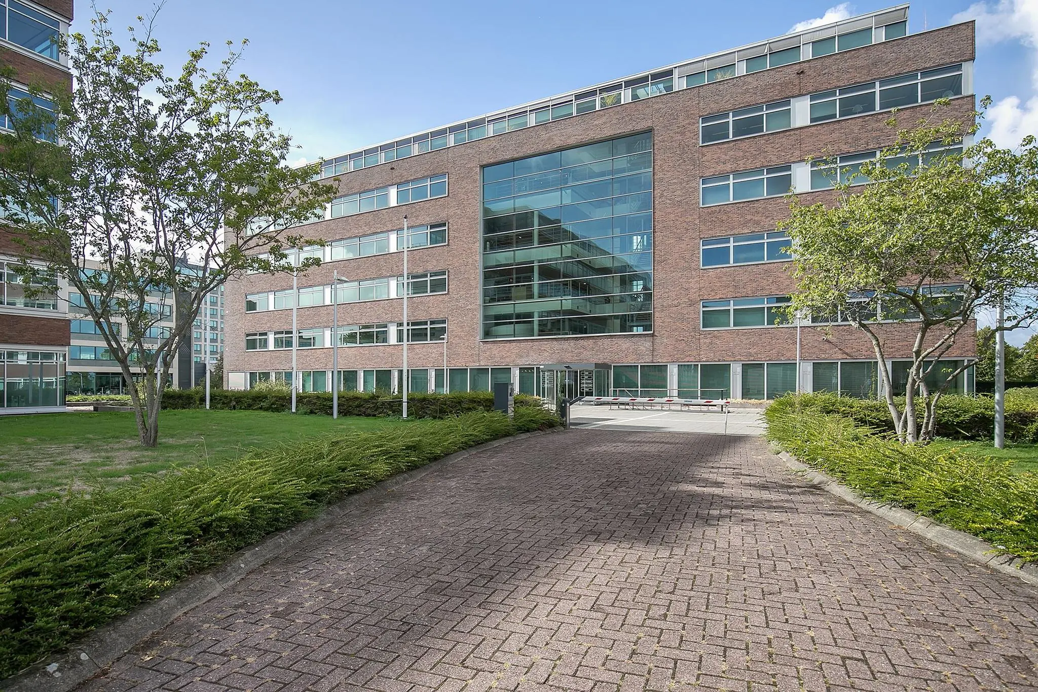 Kantoorgebouw aan de Tupolevlaan met bakstenen gevel, grote glazen entree en omliggende groenvoorziening.