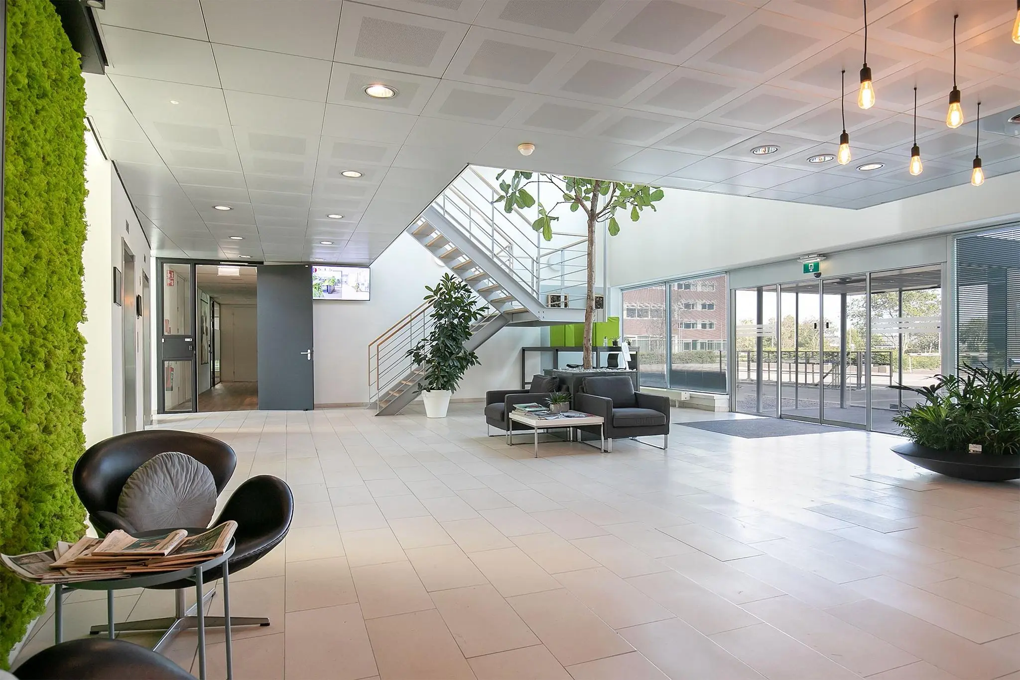 Moderne, lichte entreehal van een kantoorpand aan de Tupolevlaan met zithoek, planten en een trap naar boven.