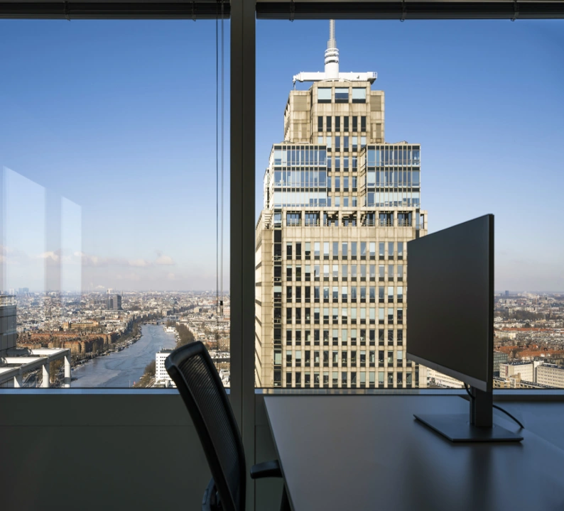 Uitzicht vanuit een modern kantoor met bureaustoel en monitor op de Rembrandt Tower aan het Amstelplein in Amsterdam.