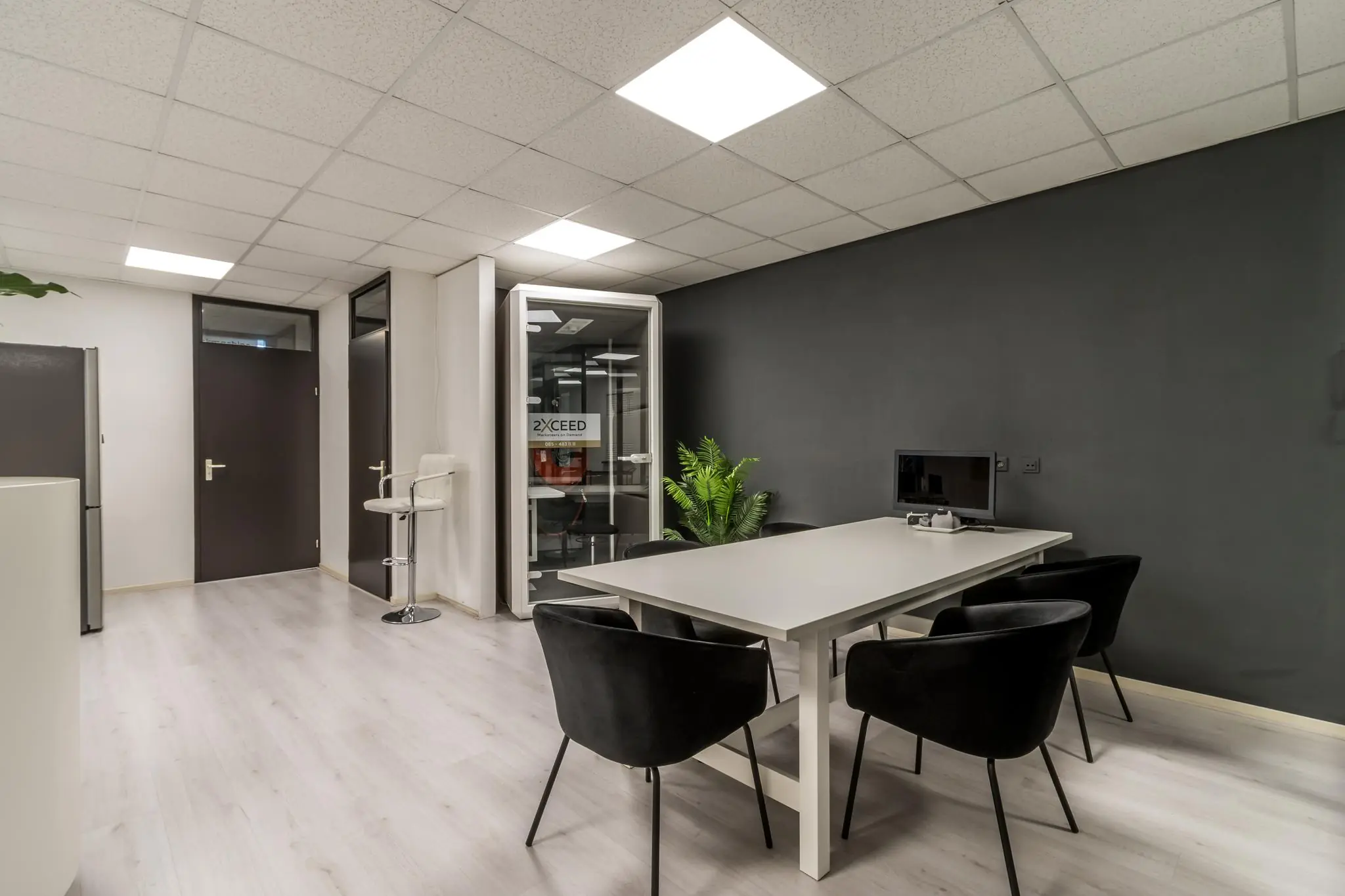 Moderne kantoorruimte aan de Koningsweg met een vergadertafel, zwarte stoelen, een computer en een aparte belcel van 2XCEED.