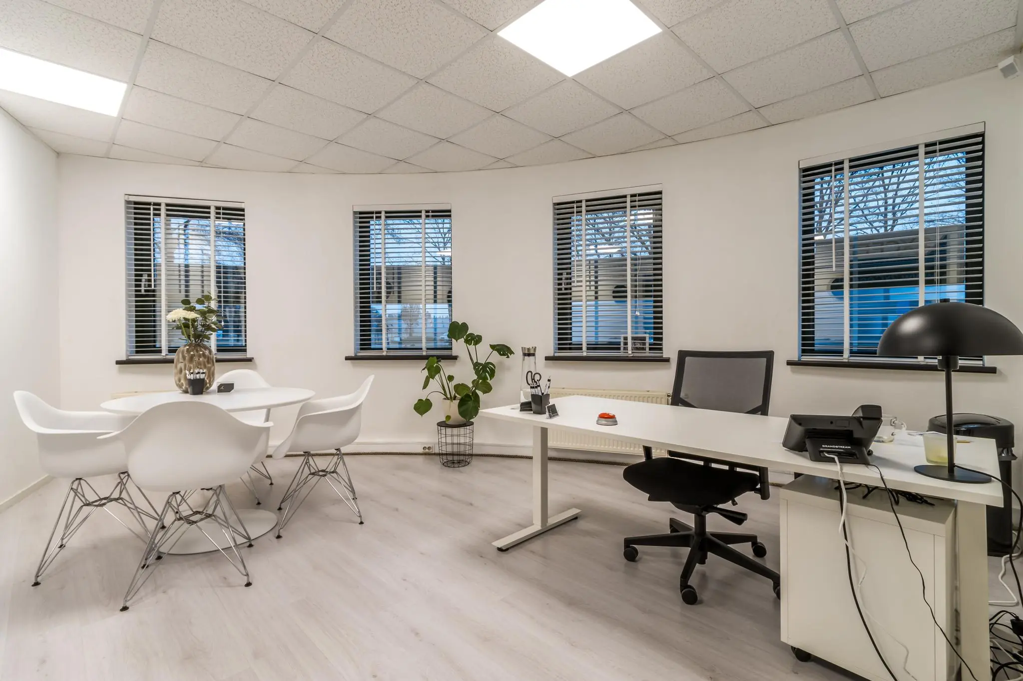 Modern ingerichte kantoorruimte aan de Koningsweg met een bureau, vergadertafel en vijf ramen met jaloezieën.