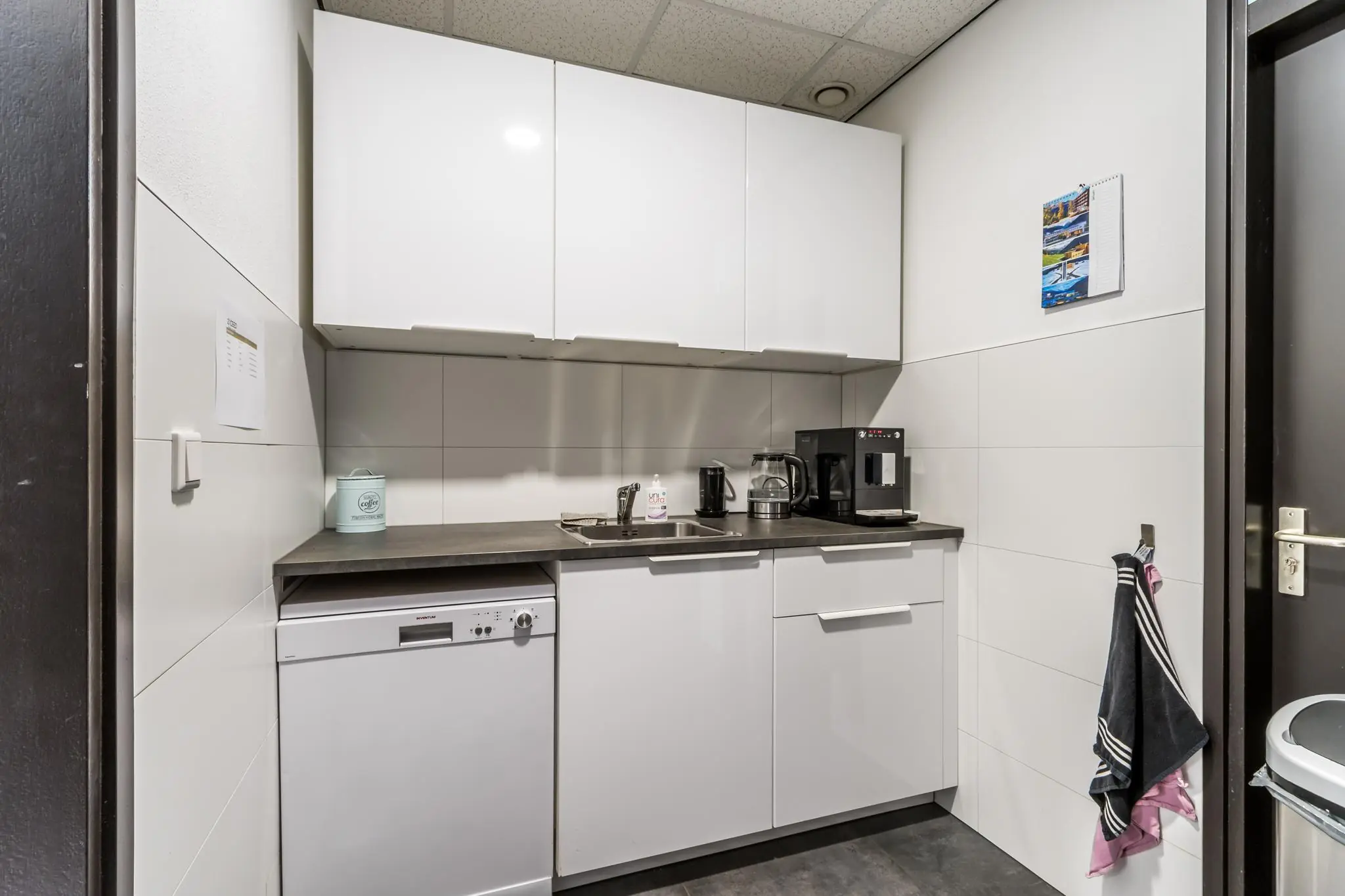 Moderne pantry met witte kasten, een koffiezetapparaat, vaatwasser en spoelbak aan de Koningsweg.