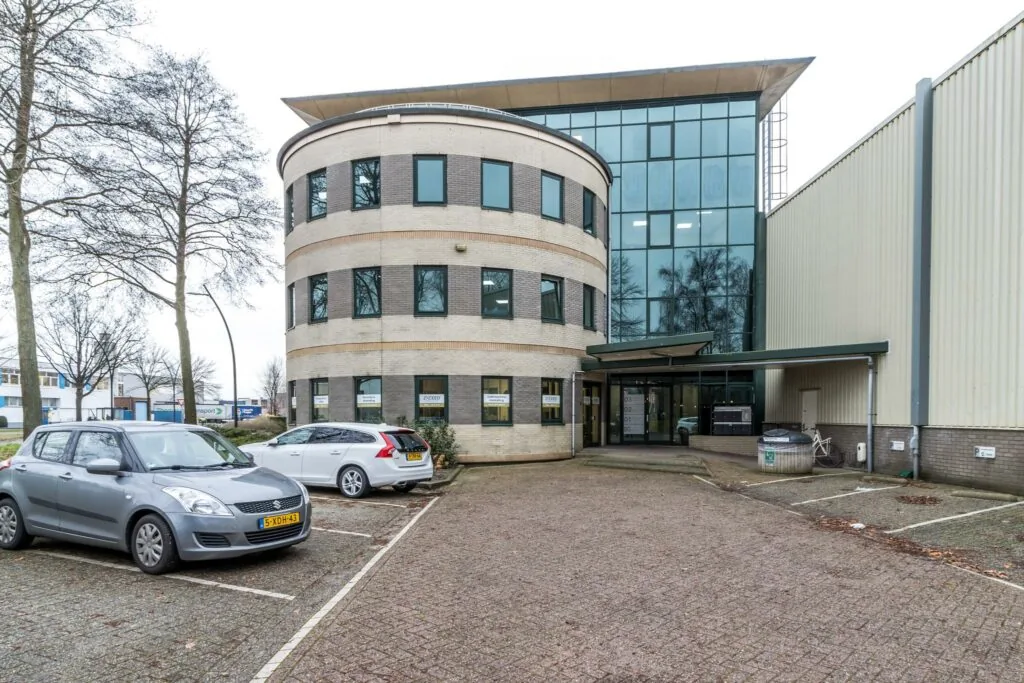 Modern kantoorgebouw aan de Koningsweg met parkeerplaatsen en auto's op de voorgrond.