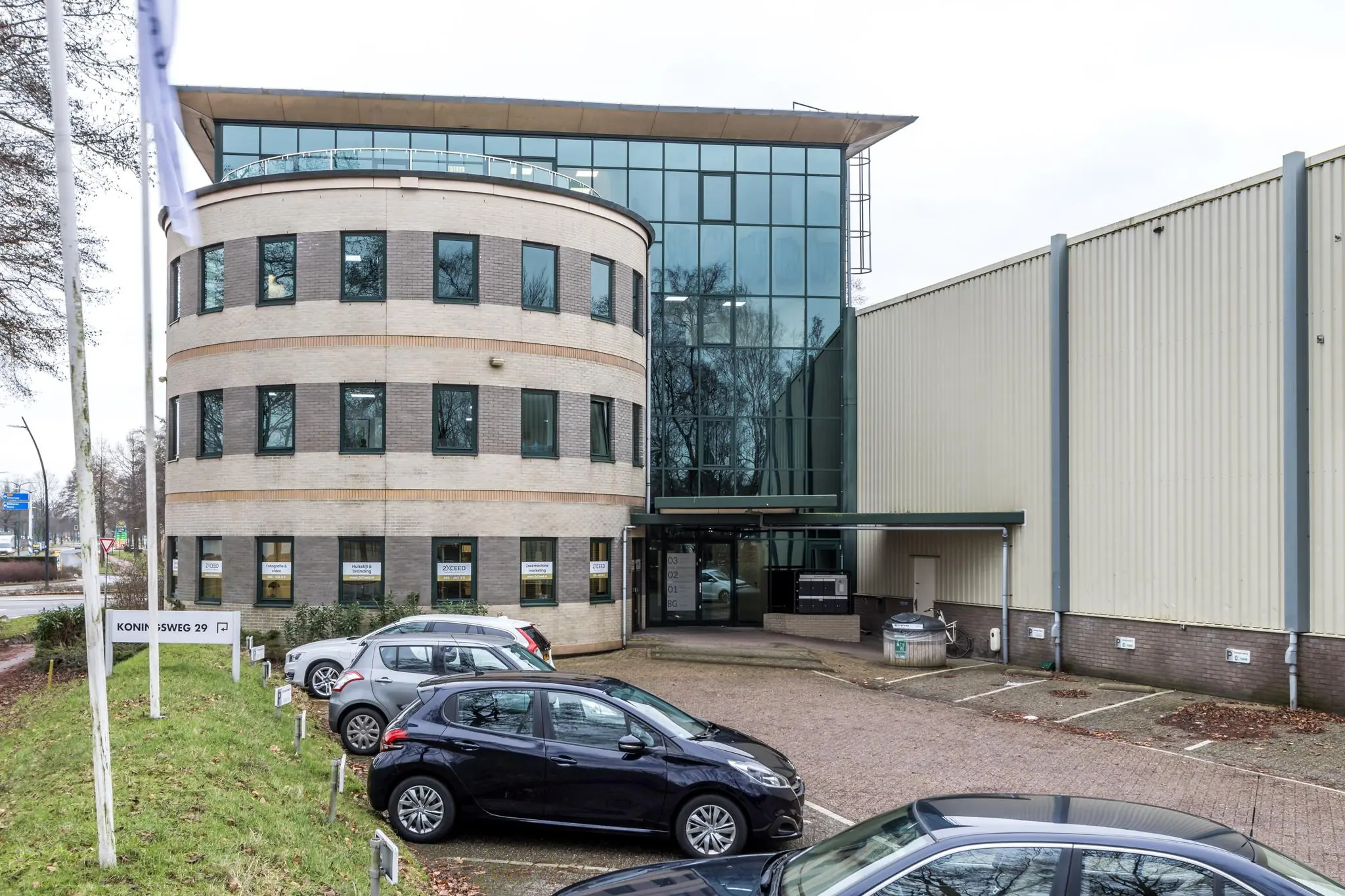 Kantoorpand aan de Koningsweg 29 met parkeervakken en meerdere geparkeerde auto's op de voorgrond.