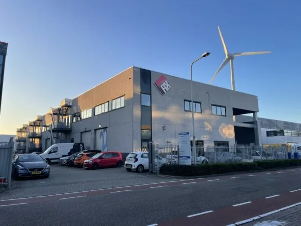Bedrijfspand van Leemidden met geparkeerde auto's, een windmolen op de achtergrond en het logo van Fix op de gevel.