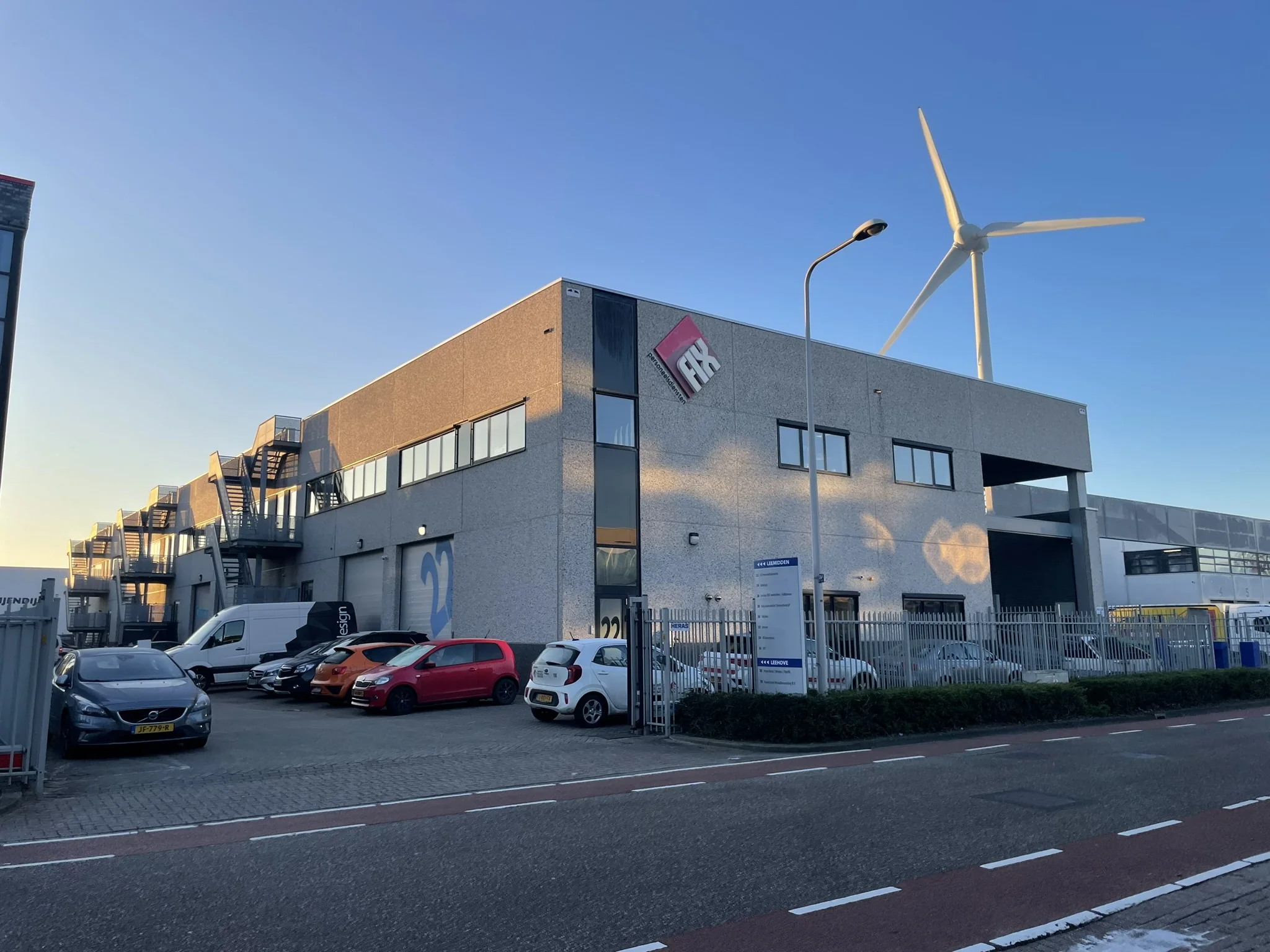 Bedrijfspand van Leemidden met geparkeerde auto's, een windmolen op de achtergrond en het logo van Fix op de gevel.