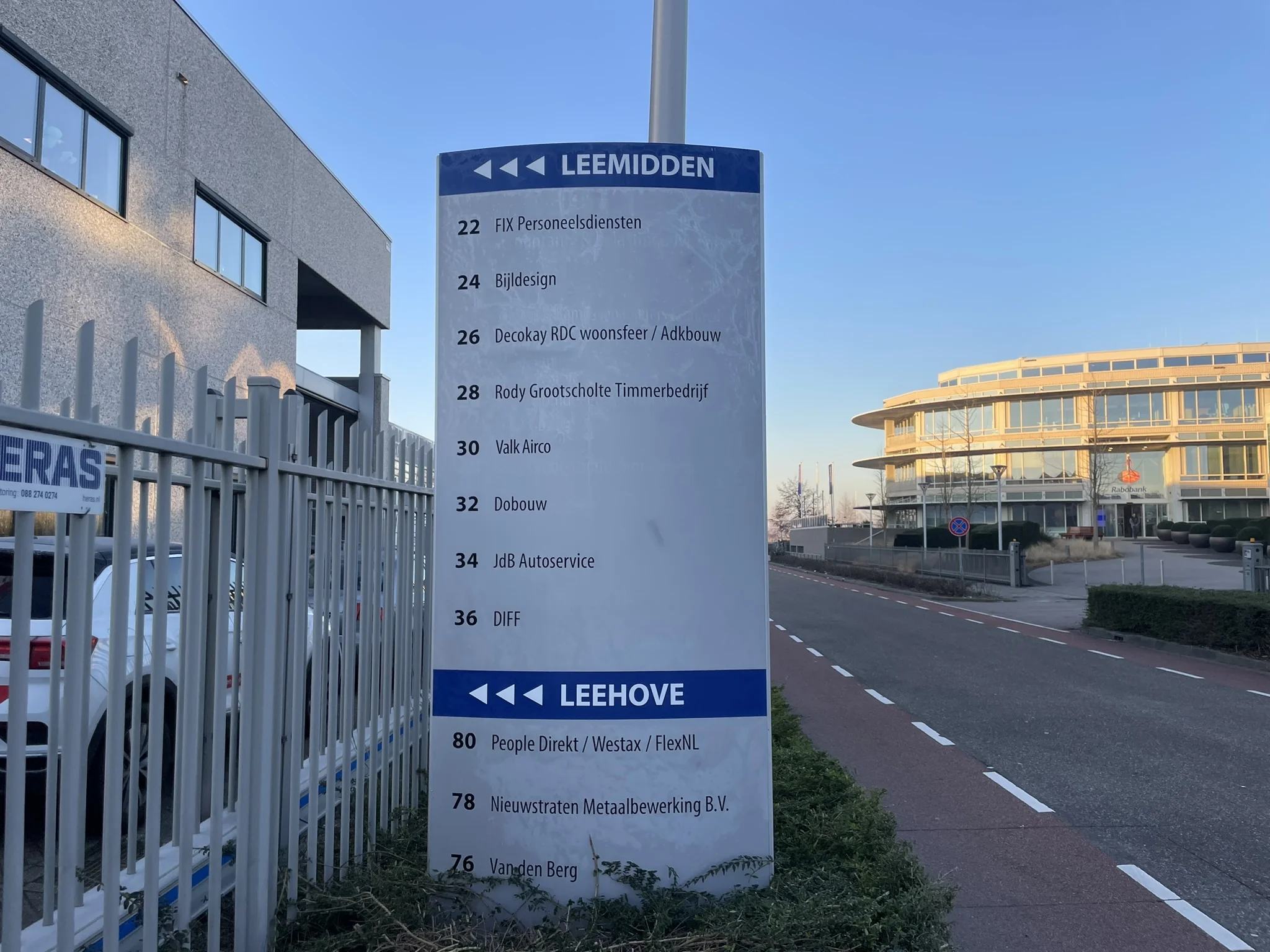 Wegwijzer met bedrijfsnamen en huisnummers op bedrijventerrein Leemidden en Leehove in een stedelijke omgeving.