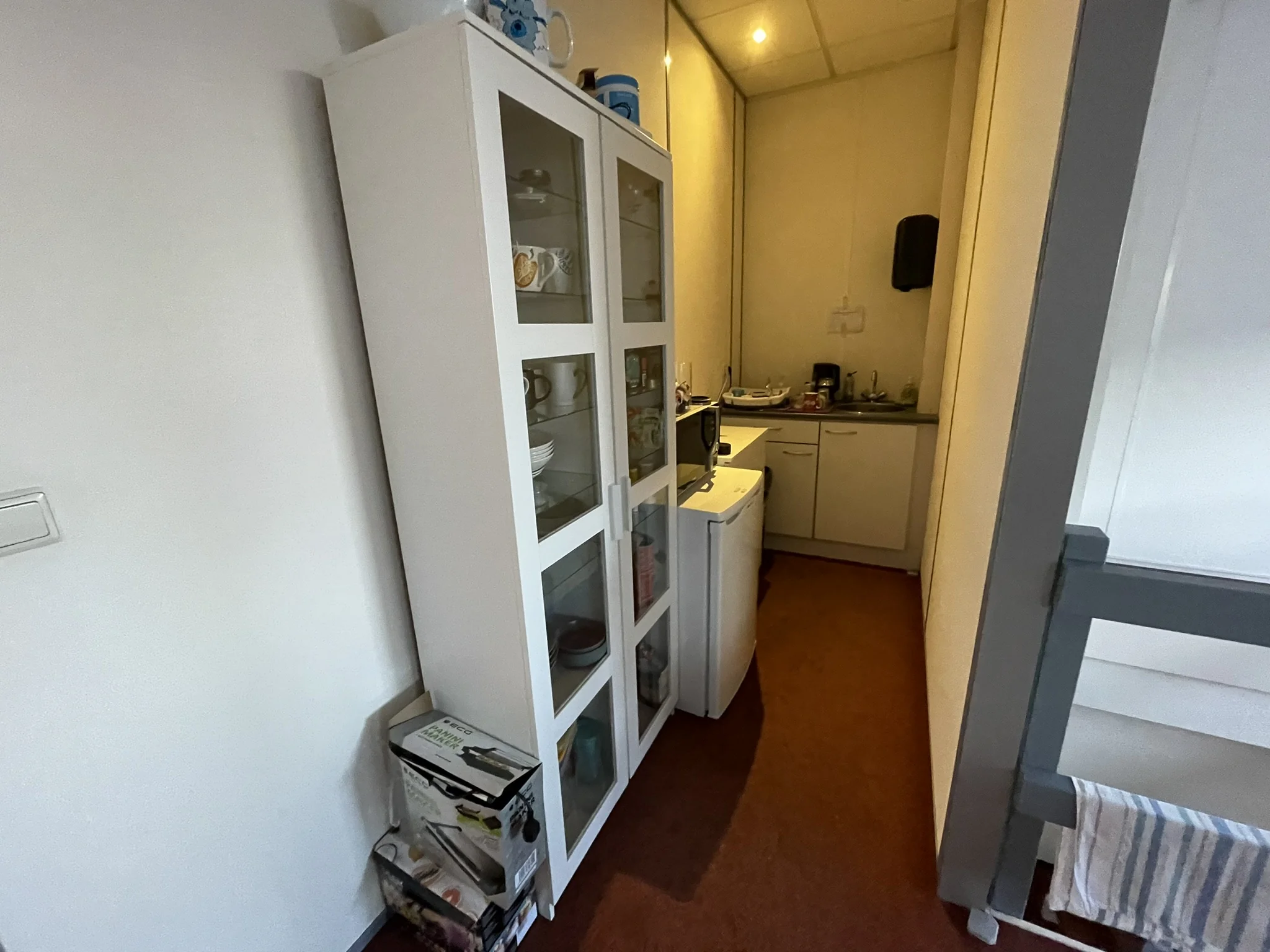 Kleine smalle keuken met witte kasten, servieskast, koelkast en aanrecht met keukengerei.