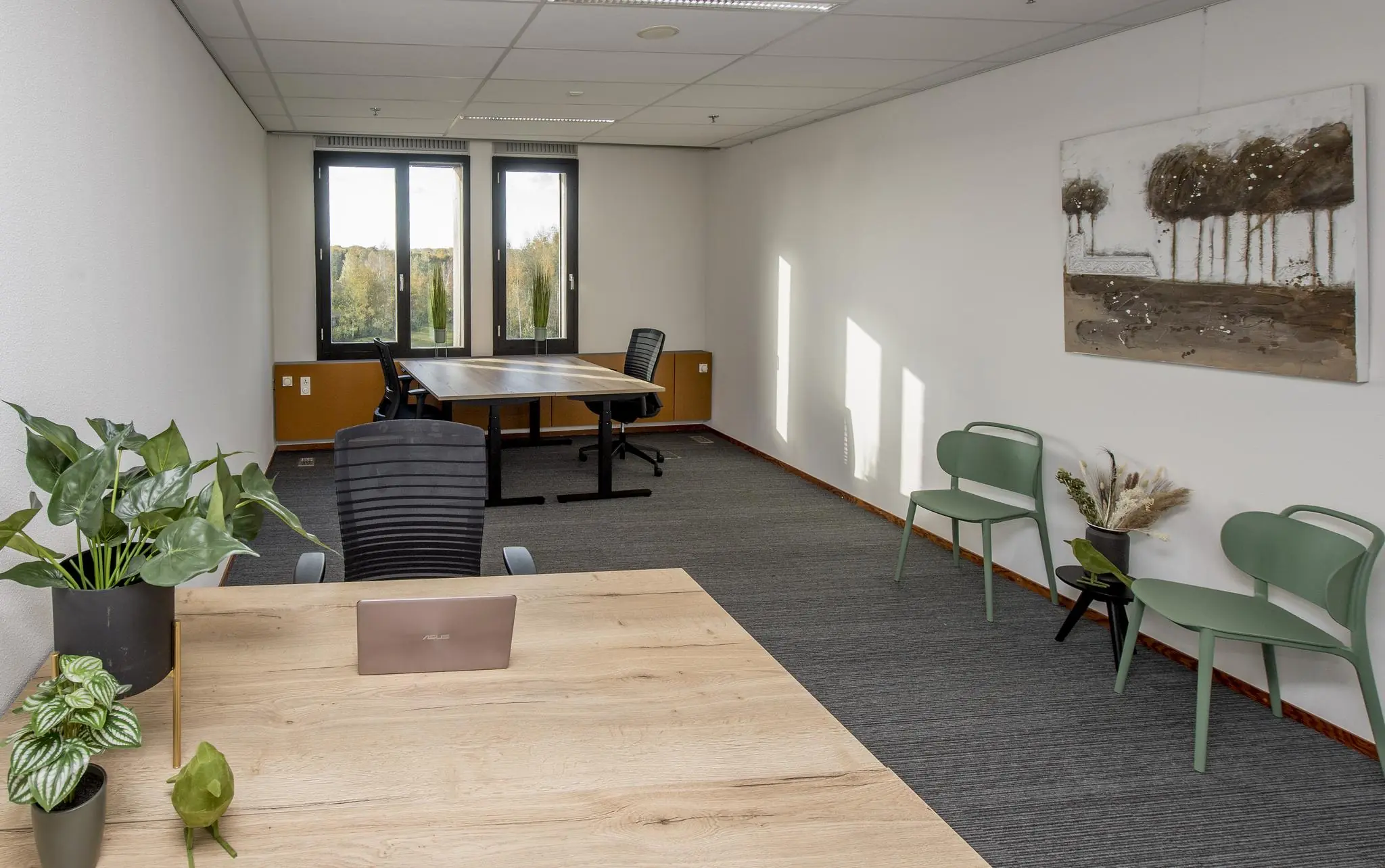 Modern kantoorinterieur aan de Fokkerstraat met houten bureaus, groene stoelen, kamerplanten en een groot raam met uitzicht op bomen.