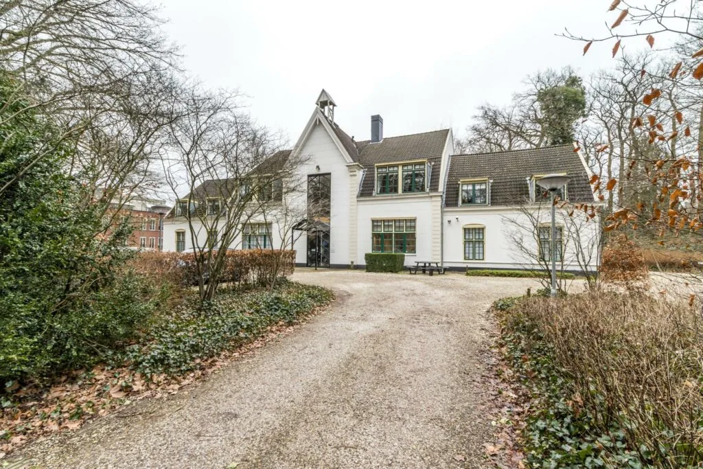 Witte villa aan de Driebergseweg omgeven door bomen en een grindpad.