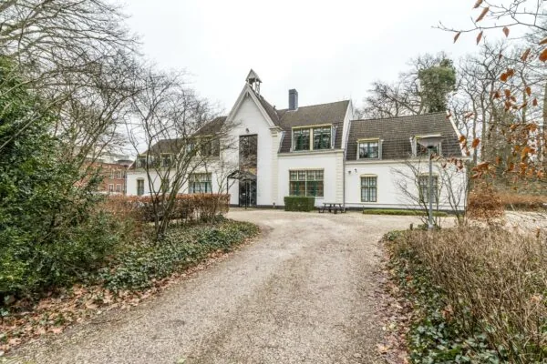 Witte villa aan de Driebergseweg omgeven door bomen en een grindpad.