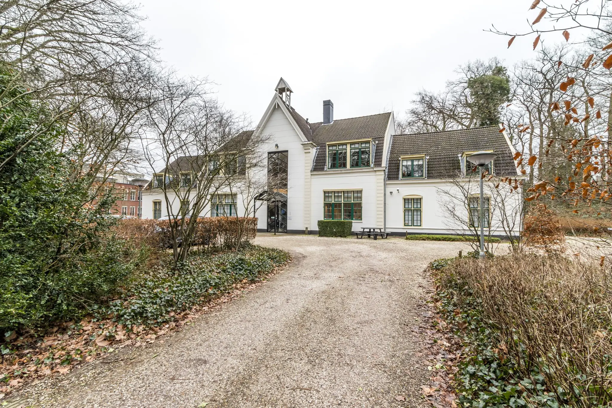 Witte villa aan de Driebergseweg omgeven door bomen en een grindpad.