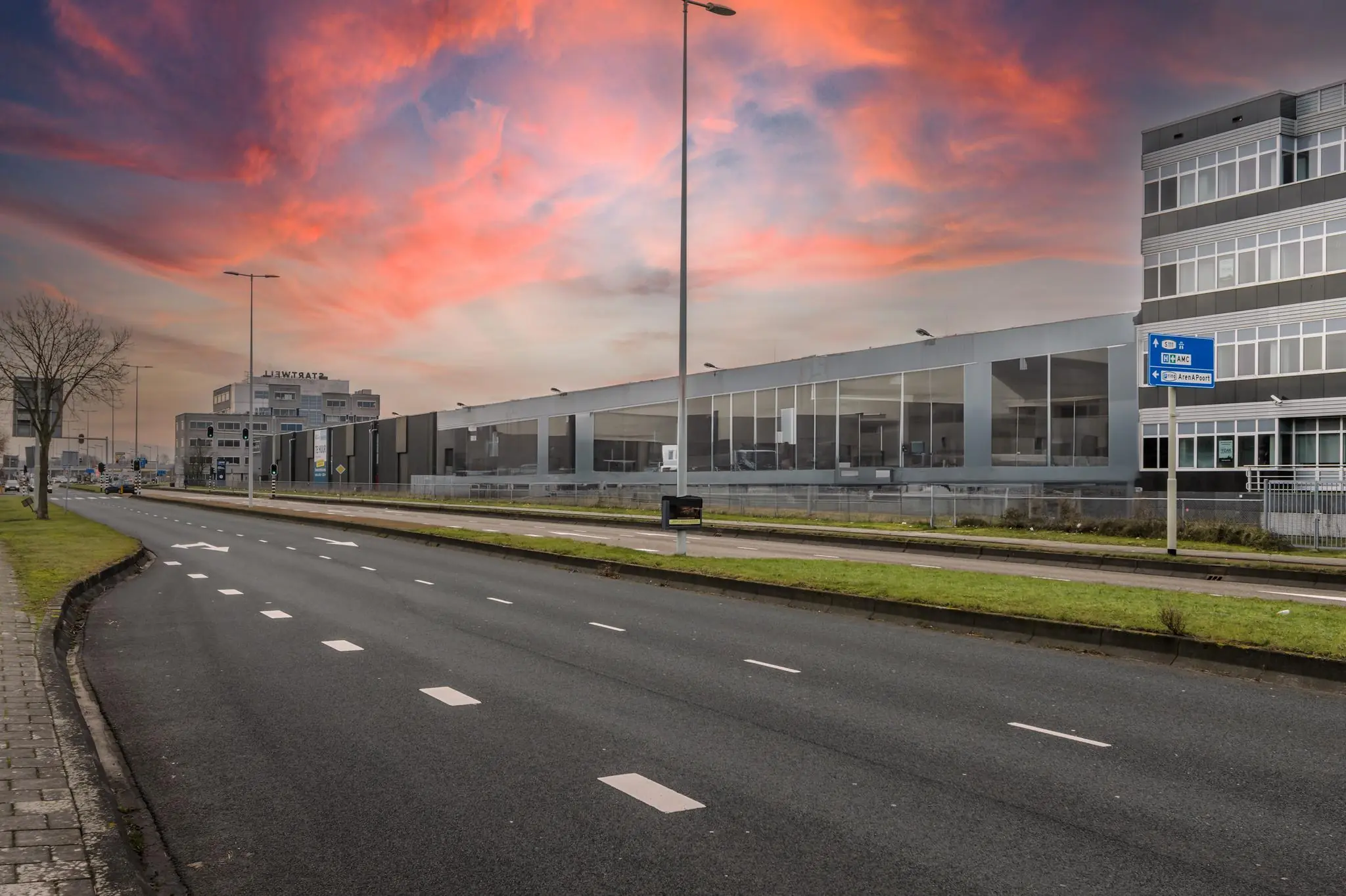 Lemerlerbergweg in Amsterdam met kantoorgebouwen en een kleurrijke zonsondergang aan de horizon.