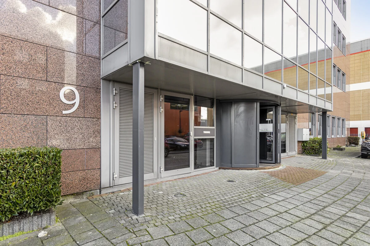 Ingang van een modern kantoorpand aan de Curieweg 9 met een draaiende toegangsdeur en spiegelende gevel.