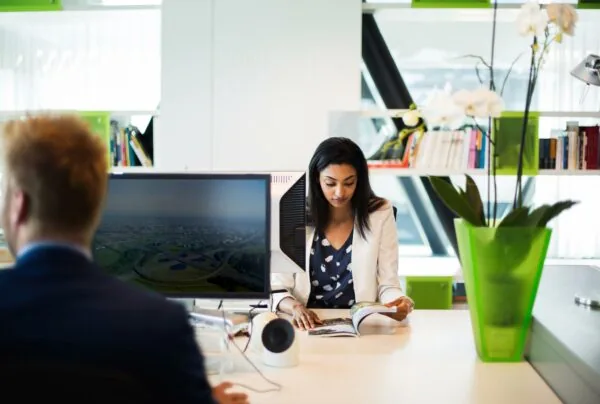 Twee mensen werken op een modern kantoor aan de Orteliuslaan, met een vrouw die een tijdschrift leest en een man achter een computerscherm.