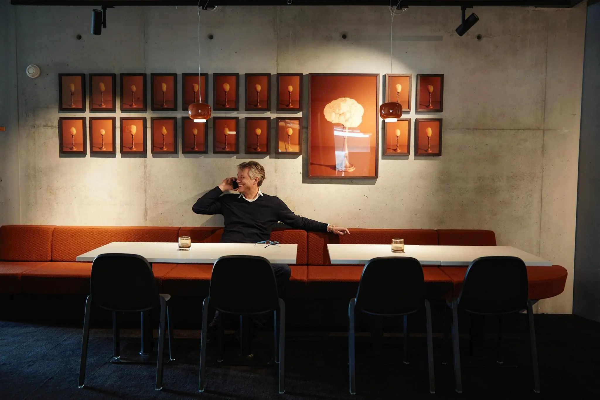 Man zit lachend aan een tafel en belt in een modern ingericht kantoor aan de Orteliuslaan, met kunstwerken van groente op de achtergrond.