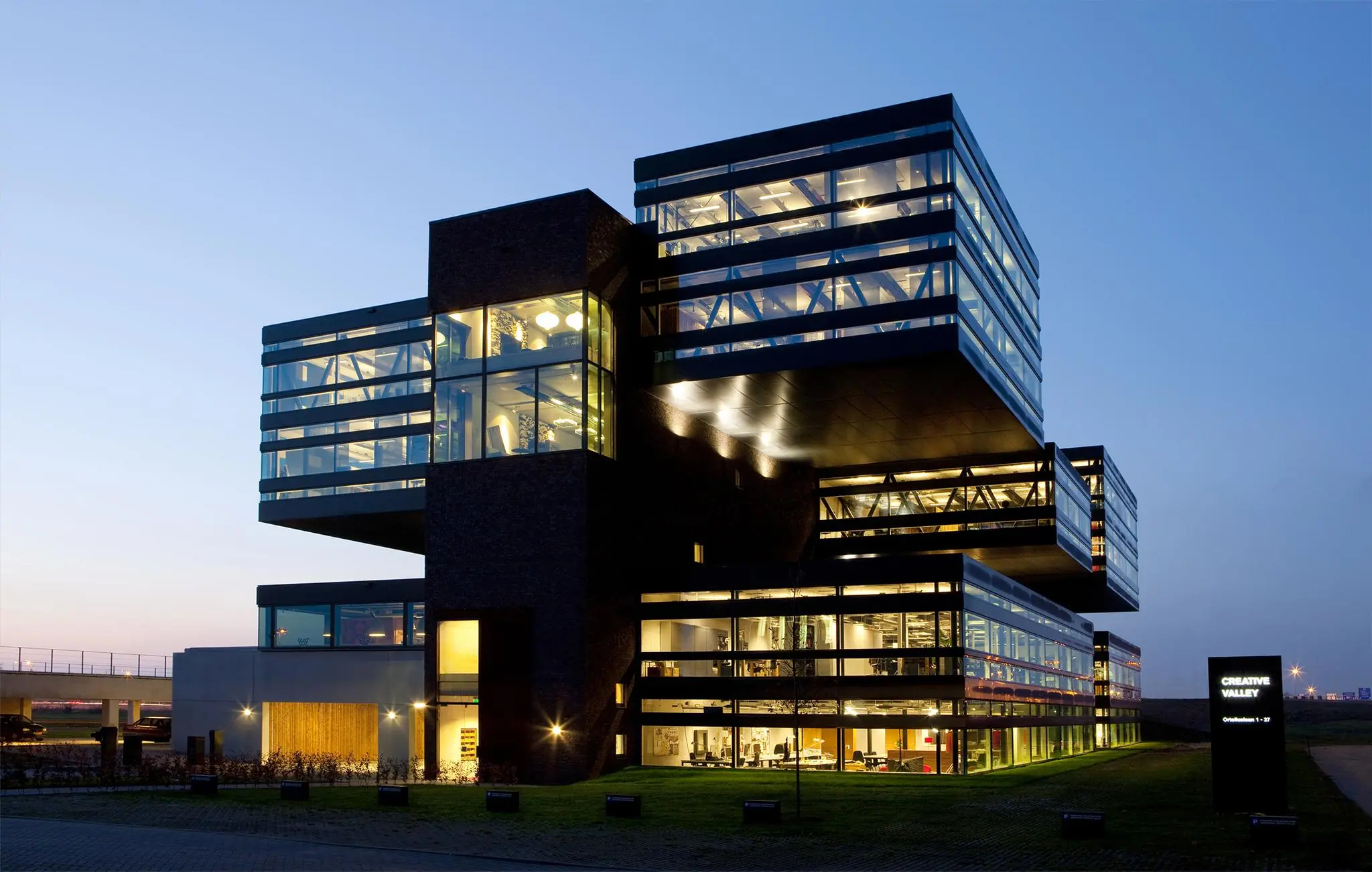 Modern kantoorgebouw Creative Valley aan de Orteliuslaan, verlicht in de avondschemering.