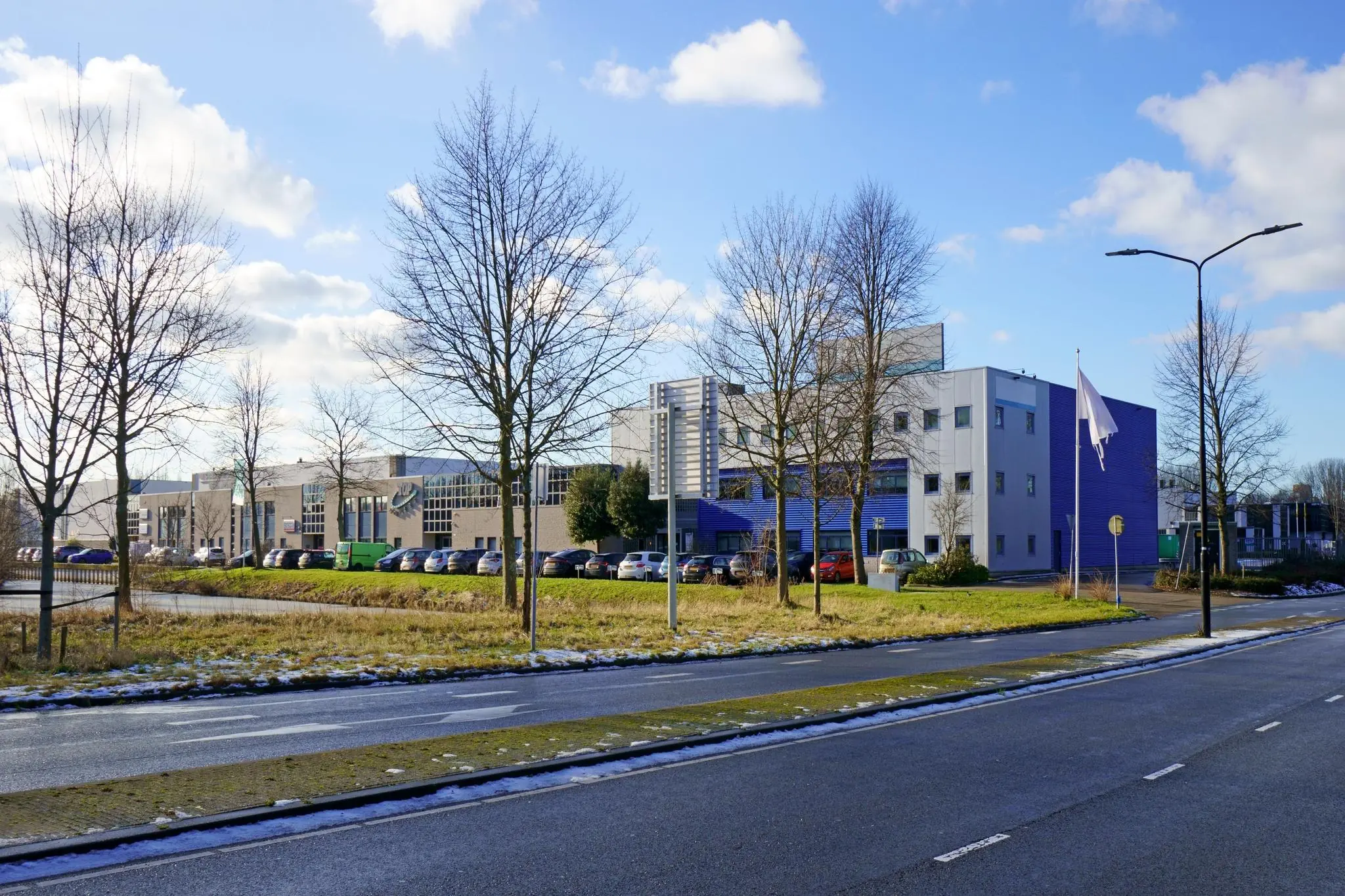 Bedrijventerrein aan de Zuiderweg met moderne kantoorgebouwen, geparkeerde auto's en een lege vlaggenmast op een zonnige winterdag.