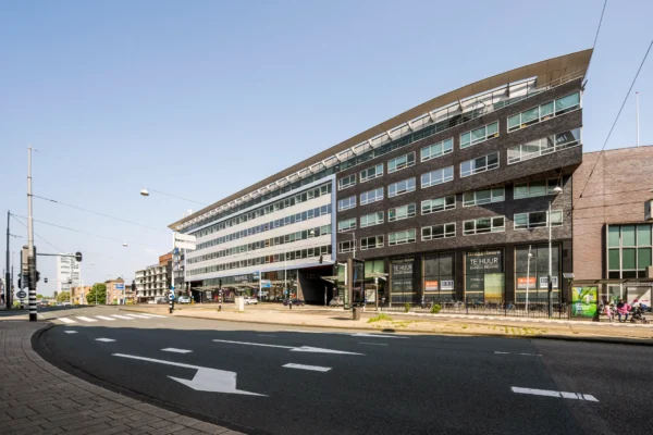 Straatbeeld met een modern kantoorgebouw aan een drukke weg, met verschillende borden die kantoorruimte te huur aanbieden.