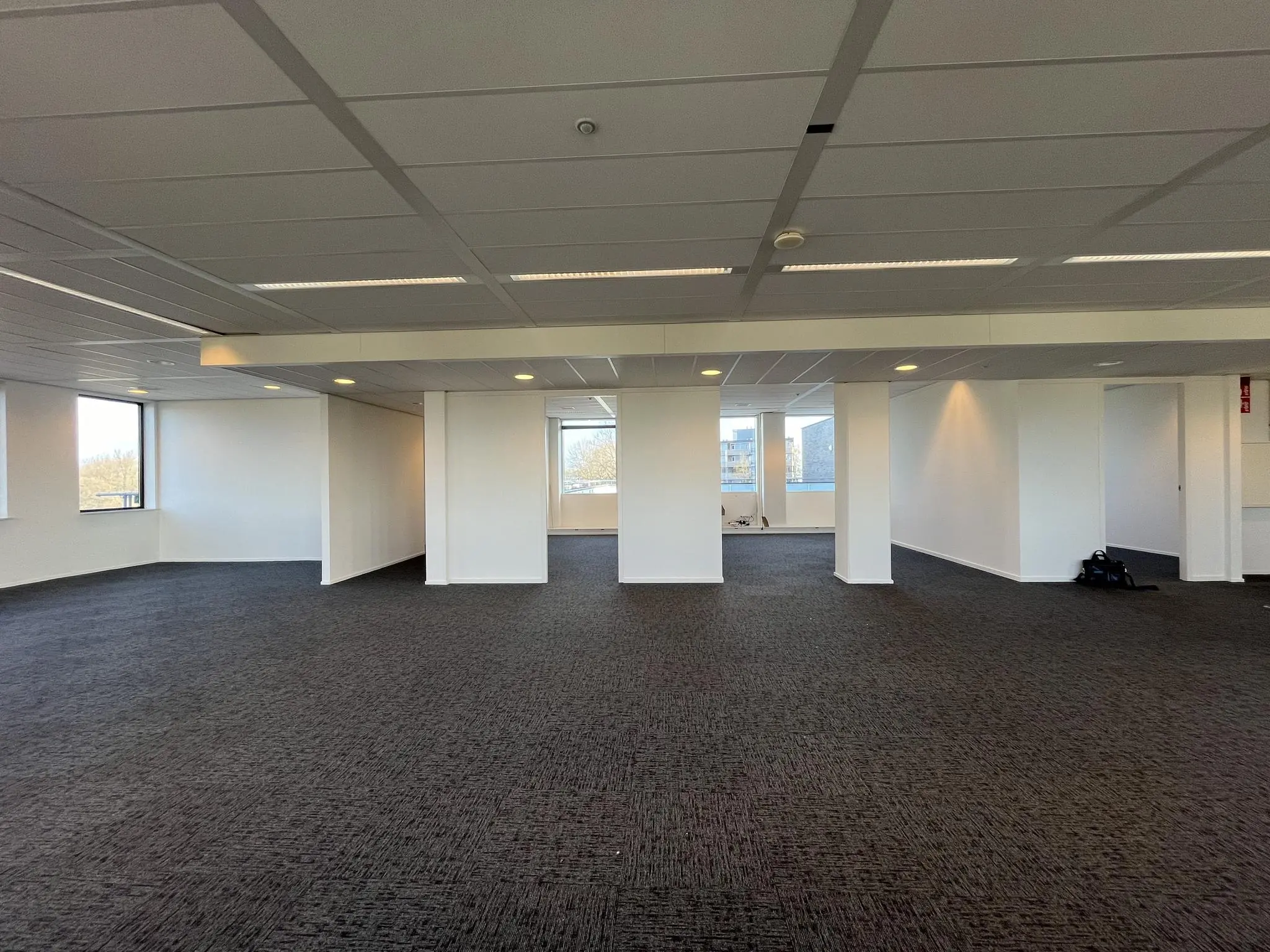 Lege kantoorruimte met witte muren, systeemplafond en donkere vloerbedekking aan de Ratelaar.