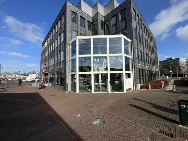 Modern kantoorgebouw De Ratelaar met glazen entree en huisnummers 39-42, gelegen aan een plein op een zonnige dag.