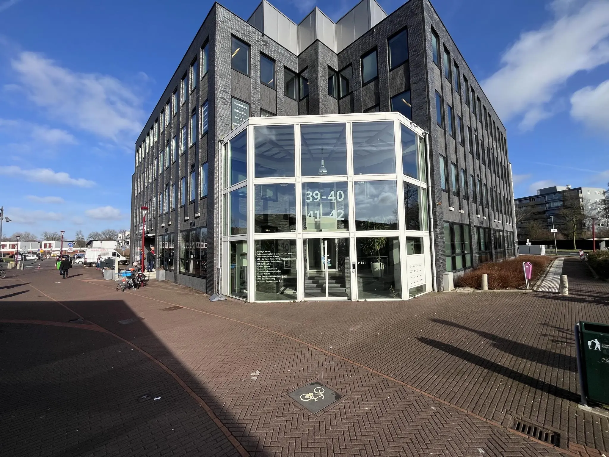 Modern kantoorgebouw De Ratelaar met glazen entree en huisnummers 39-42, gelegen aan een plein op een zonnige dag.