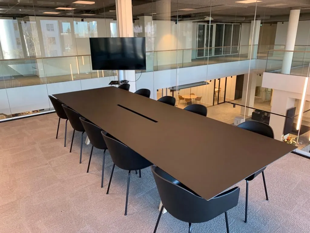 Vergaderruimte in Rijnzathe met een lang zwart conferentietafel, omringd door zwarte stoelen en een flatscreen aan de muur.