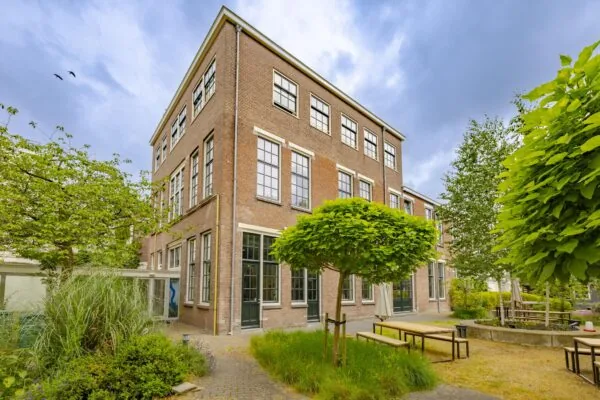 Binnenplaats met zitbanken en groene begroeiing bij een historisch bakstenen pand aan de Plantage Middenlaan.
