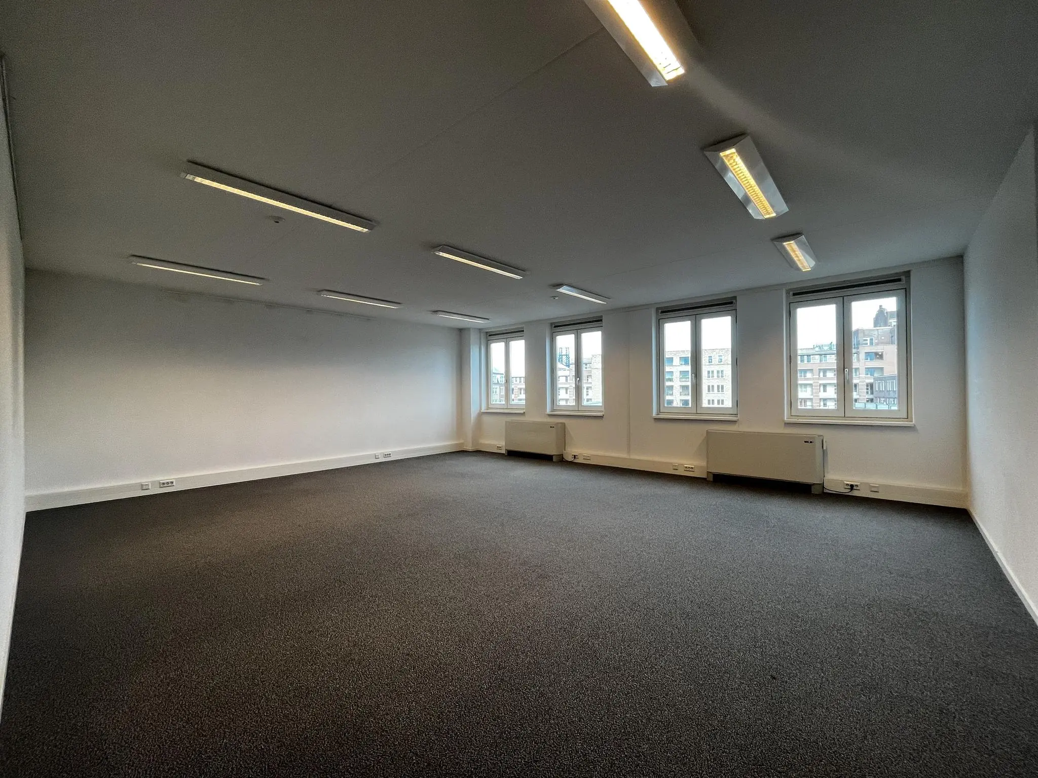 Lege kantoorruimte in gebouw Middenburcht met tapijtvloer, systeemplafond en meerdere ramen met uitzicht op de stad.
